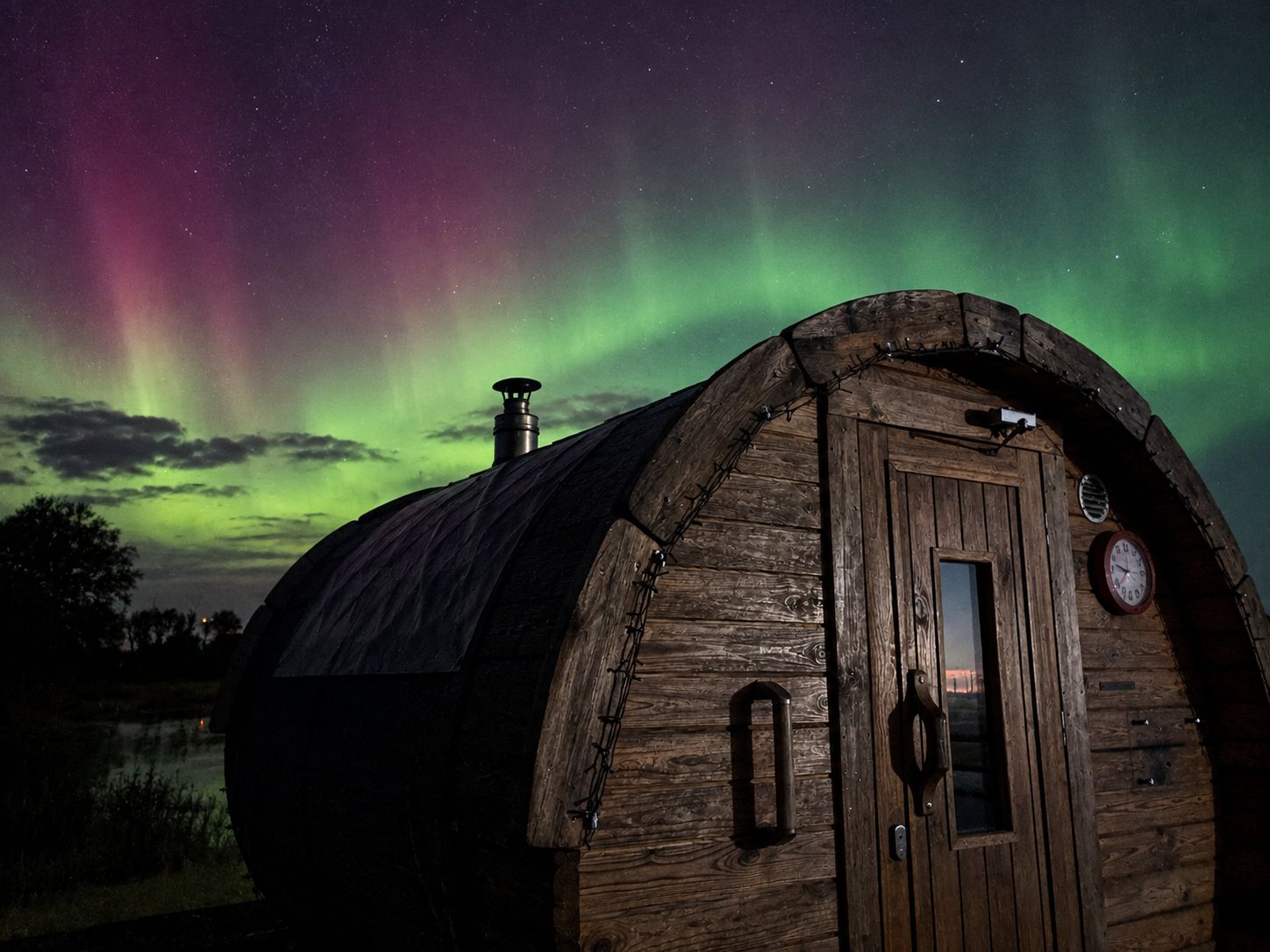 The Northern Lights glowing over the barrel sauna by the river