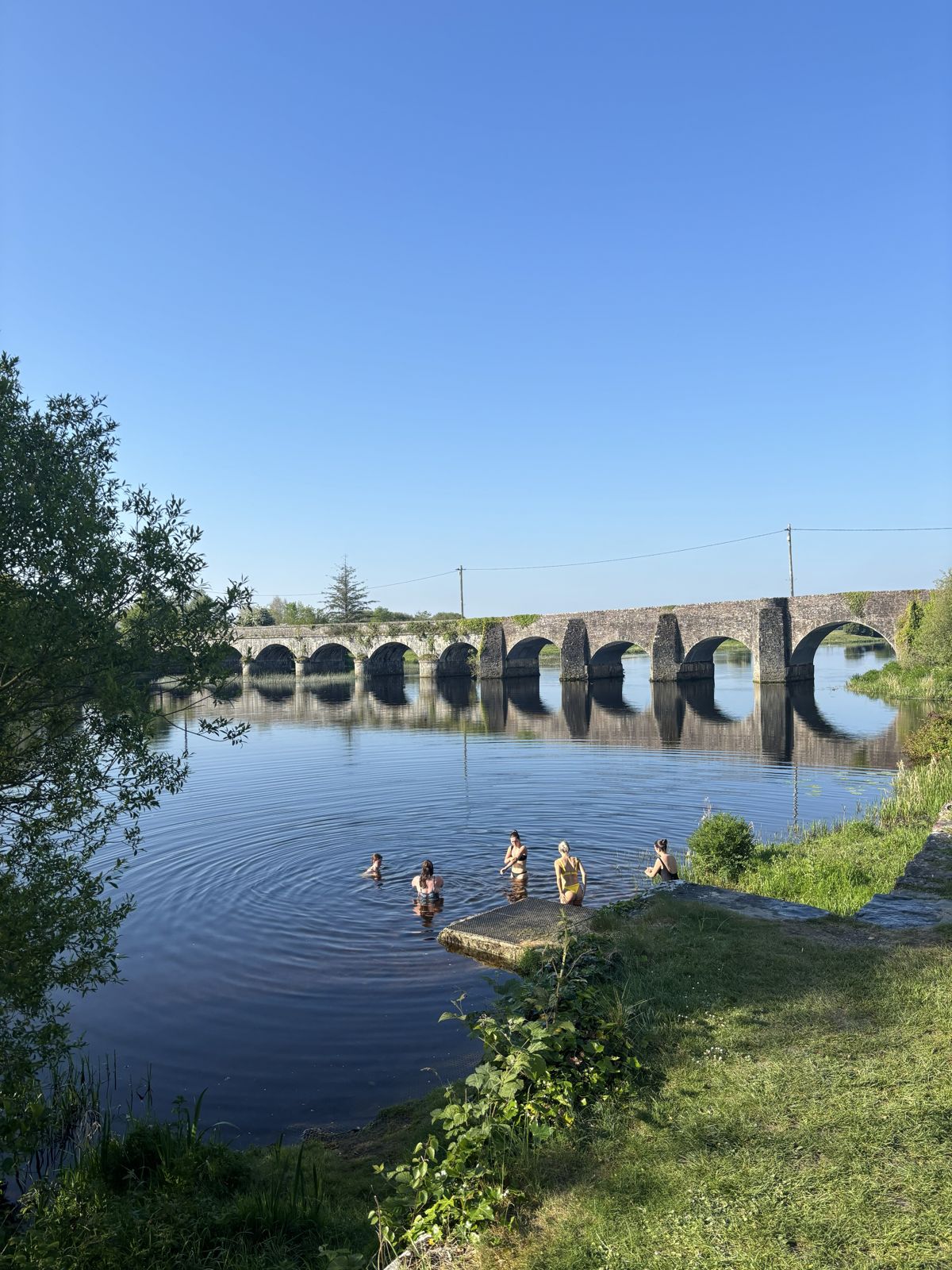 Swimmers in the river beside the stone arches of O'Brien's Bridge